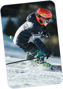 Child wearing red helmet and black ski outfit skiing downhill on snow.